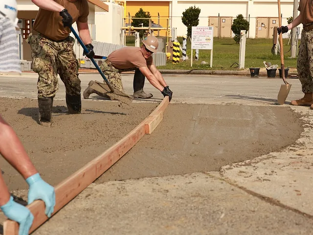 Kőművesek friss betont simítanak léccel az építkezésen
